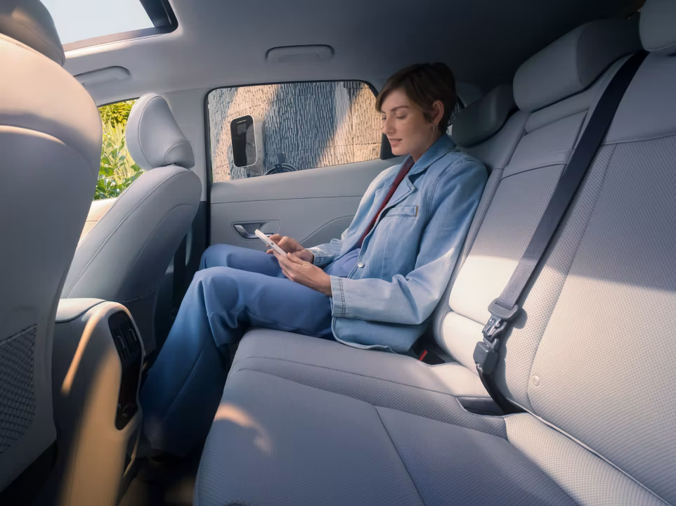 A woman using her smartphone on the back seat of the Hyundai KONA Electric SUV.